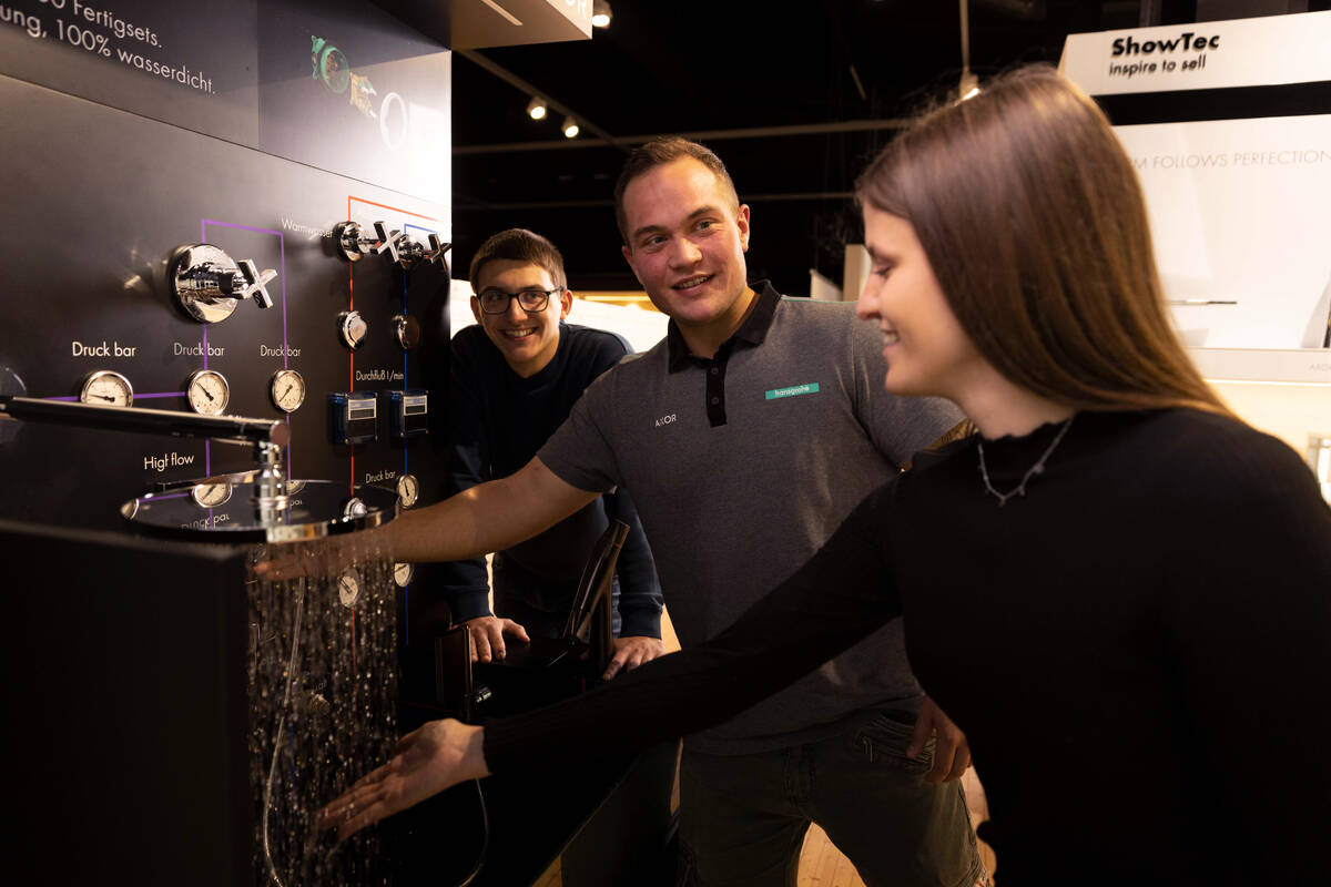 zwei Personen zeigen einer anderen Peron eine Armatur 