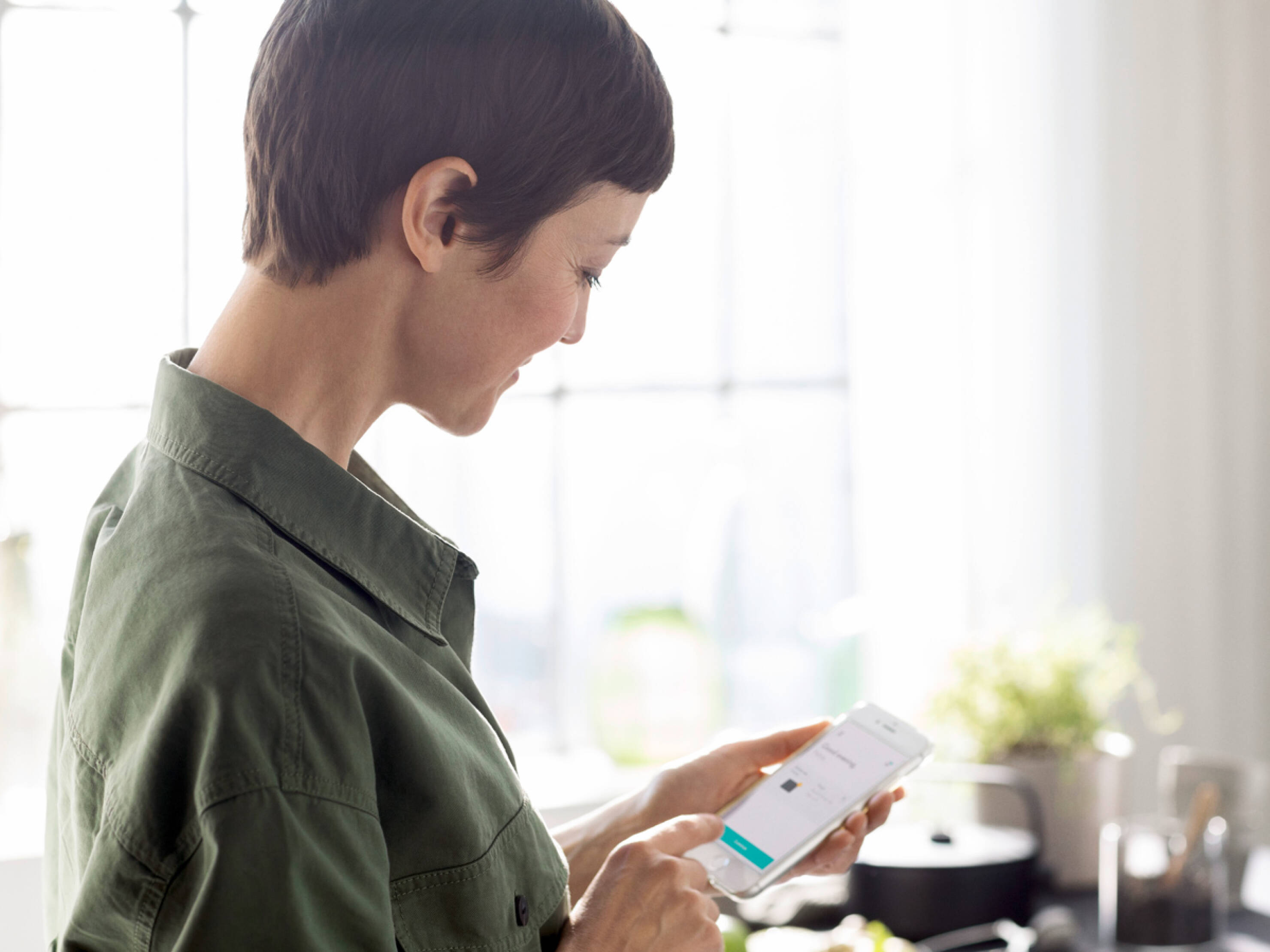 Frau bedient die hansgrohe home App am Smartphone. Frau bedient die hansgrohe home App am Smartphone.