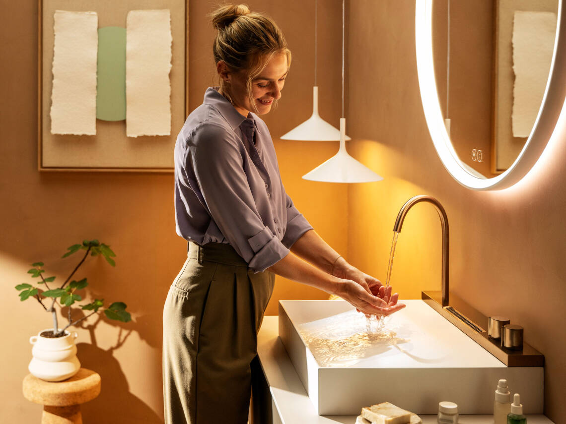 Femme au lavabo devant un miroir éclairé.