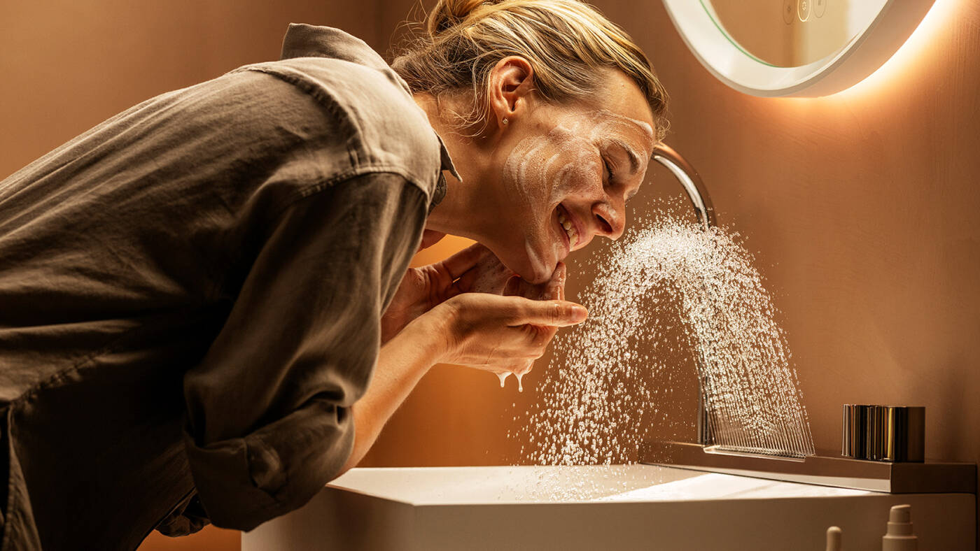 Femme radieuse se lavant le visage avec un mitigeur Avalegra.