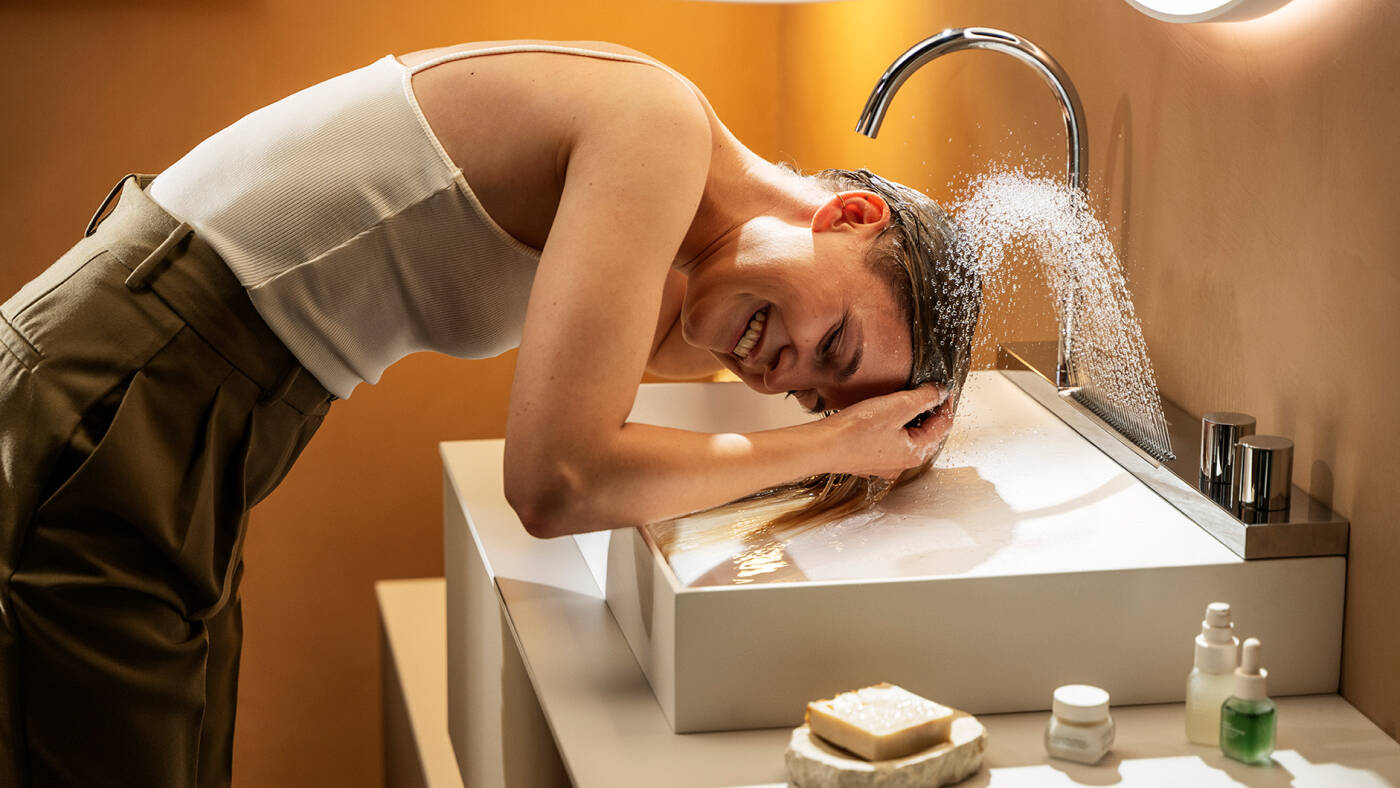 Femme se lavant les cheveux au-dessus du mitigeur de lavabo.