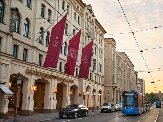 Entrance of Hotel Vier Jahreszeiten Kempinski Munich on Maximilianstrasse with signature flags and historic architecture.