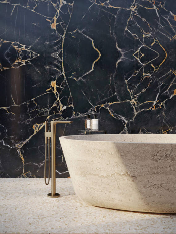 Illustration of an AXOR Citterio C floor-standing single lever bath faucet with cubic cut in Brushed Bronze, next to a modern freestanding bathtub, against an elegant black marble wall.