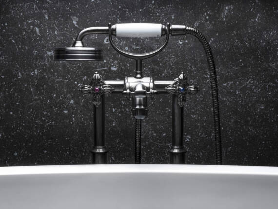 Close-up of an AXOR Montreux bathtub faucet in Brushed Black Chrome with individualized handles through AXOR Signature, against an elegant black wall, above a white bathtub