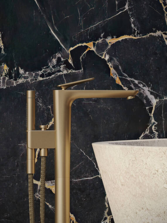 AXOR Citterio C floor-standing single lever bath mixer with cubic cut handle in Brushed Bronze, in front of an elegant black marble wall and next to a white bathtub. AXOR Citterio C floor-standing single lever bath mixer with cubic cut handle in Brushed Bronze, in front of an elegant black marble wall and next to a white bathtub.