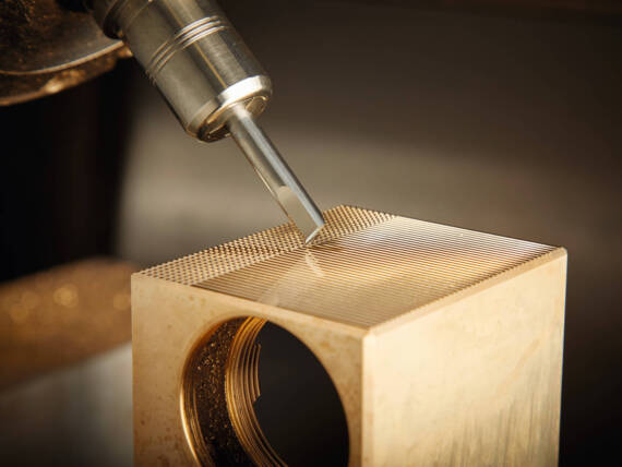 Nahaufnahme eines Präzisionswerkzeugs, das feine Linien in ein goldfarbenes Metallstück graviert.