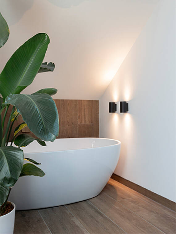 Badezimmernische mit Dachschräge, freistehender Badewanne und indirekter Beleuchtung.