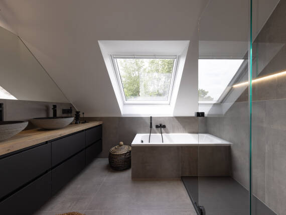 Salle de bains moderne en soupente avec baignoire et grande surface vitrée.