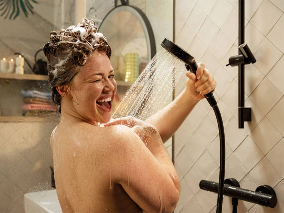 Lachende Frau duscht mit hansgrohe Pulsify in Mattschwarz.