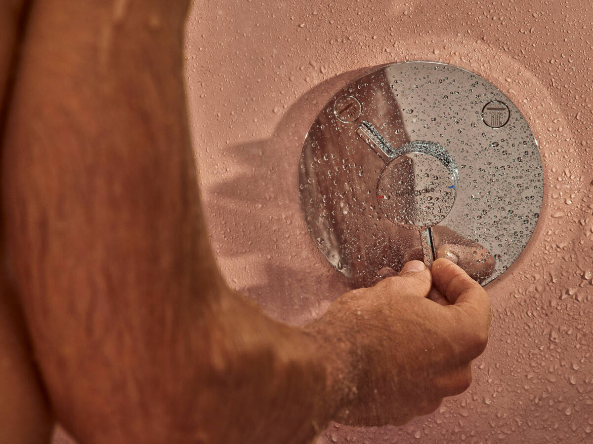 Man uses hansgrohe DuoTurn tap under the shower.