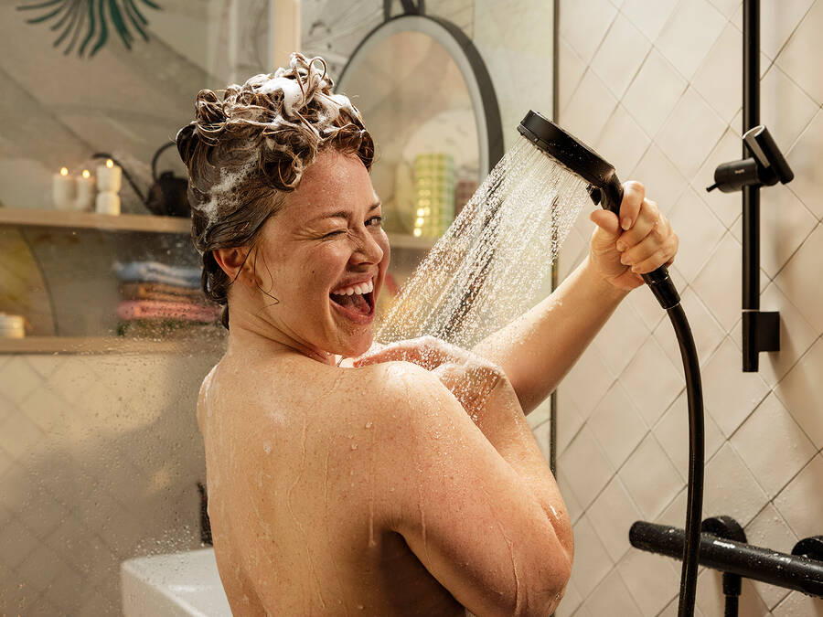 Gelukkige vrouw doucht met hansgrohe handdouche.