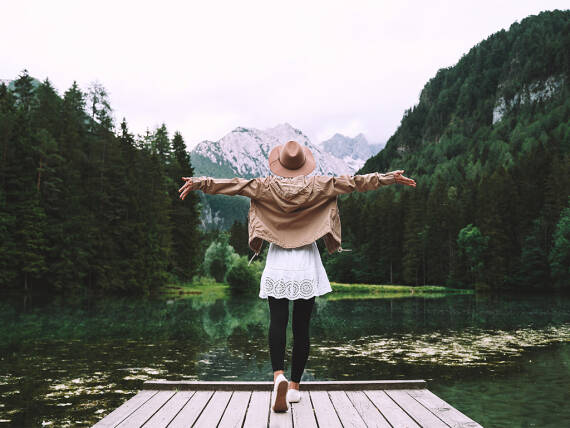 Frau in der Natur mit ausgebreiteten Armen auf einem Steg.