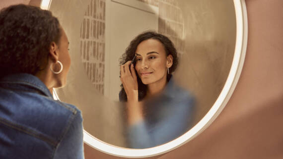Woman applying make-up in front of a mirror.