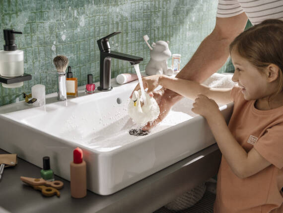 Barn, der griner ved håndvasken med en hvid badeand.