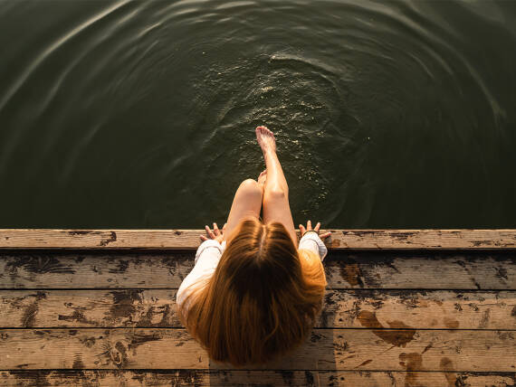 Frau sitzt auf einem Steg.