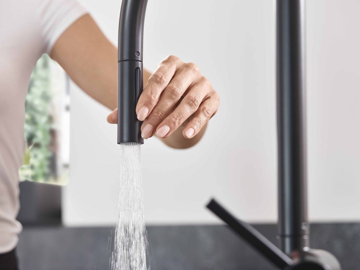 Kvinde og sprudlende vandstråle fra hansgrohe køkkenarmatur.