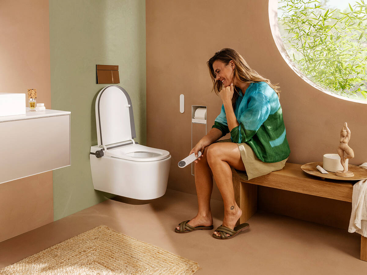 Woman operates hansgrohe shower toilet with a remote control.