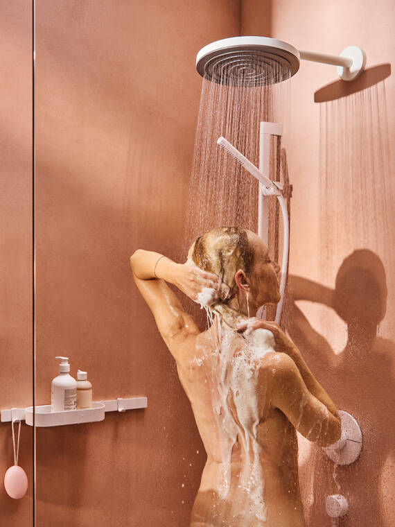 Frau spült mit Kopfbrause Shampoo aus.