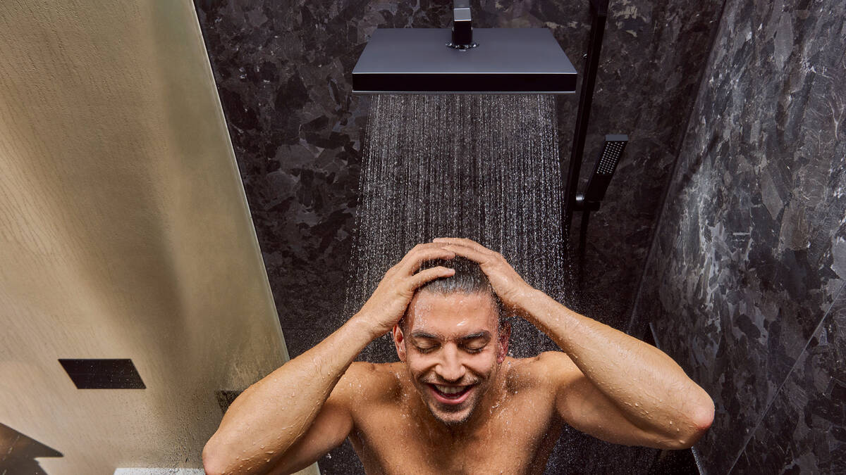 Vand strømmer fra en hovedbruser ned over hovedet og overkroppen på en mand