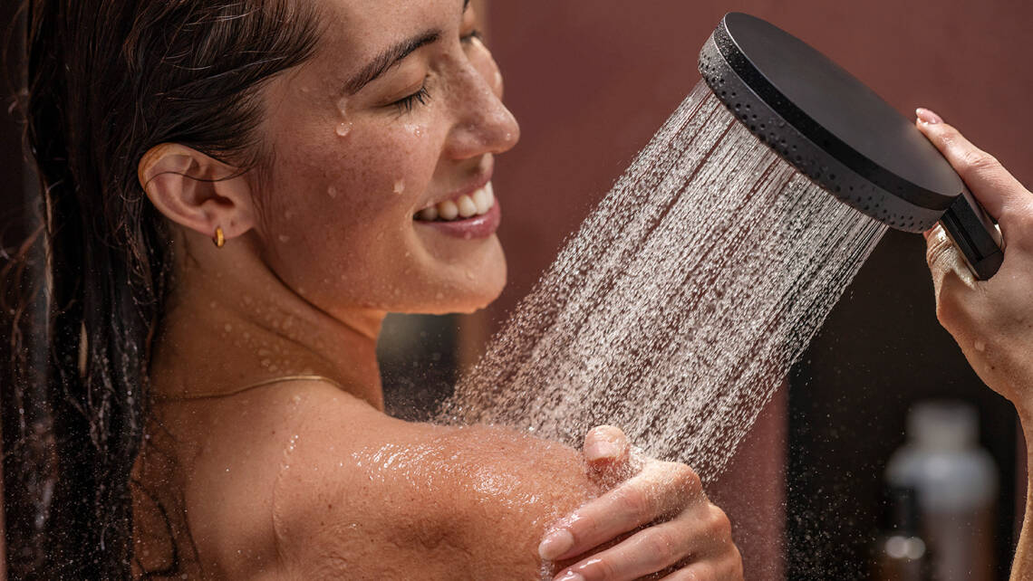 Una ragazza felice fa la doccia con una doccetta hansgrohe.