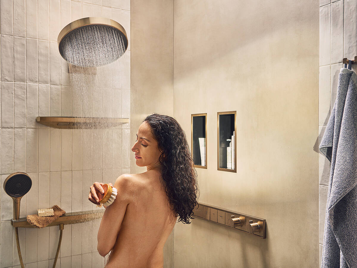 Woman showers under a large, luxurious hansgrohe shower.