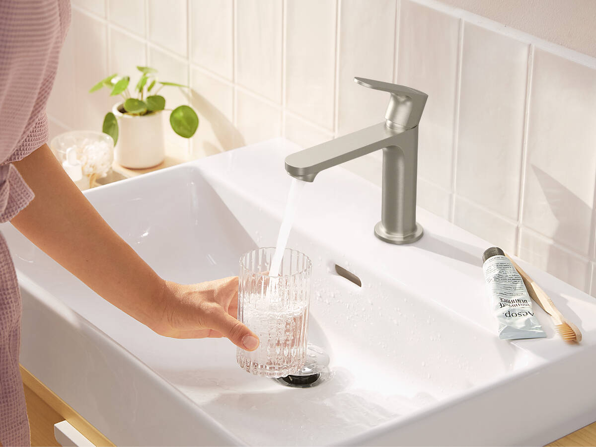 Une femme remplit un verre d'eau avec le mitigeur Rebris de hansgrohe.