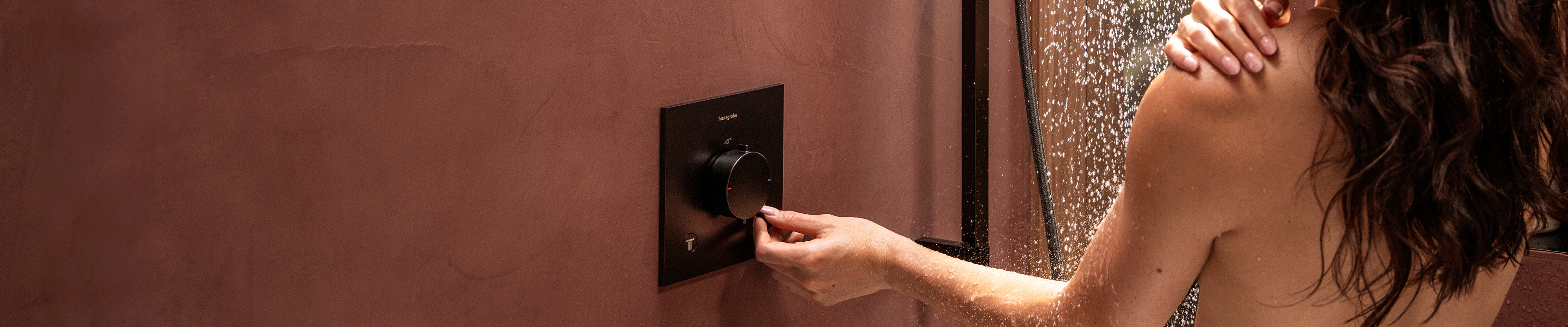 매트 블랙 컬러의 Ecostat Comfort 샤워 서모스탯을 조작하고 있는 여성의 모습.
