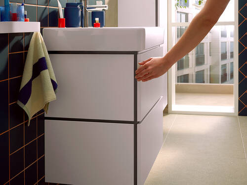 Žena otvára biely kúpeľňový nábytok Xilesa svojou nohou.