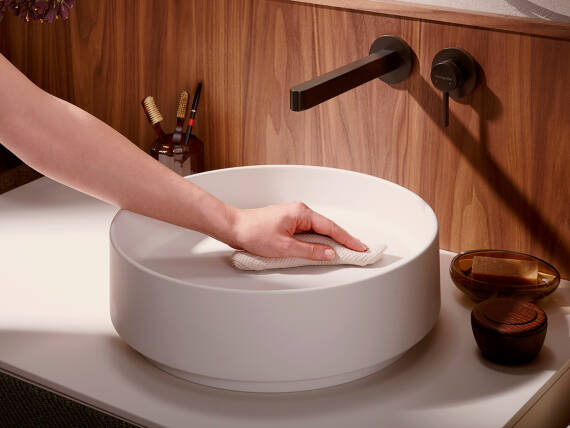 Woman's hand wiping a hansgrohe wash basin with a cloth.