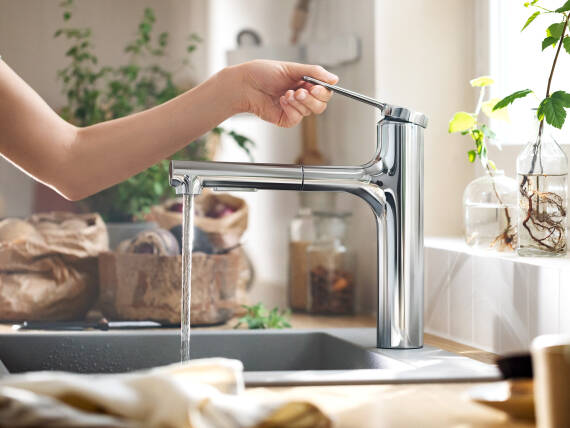 Woman operating kitchen faucet with hansgrohe water saving function.
